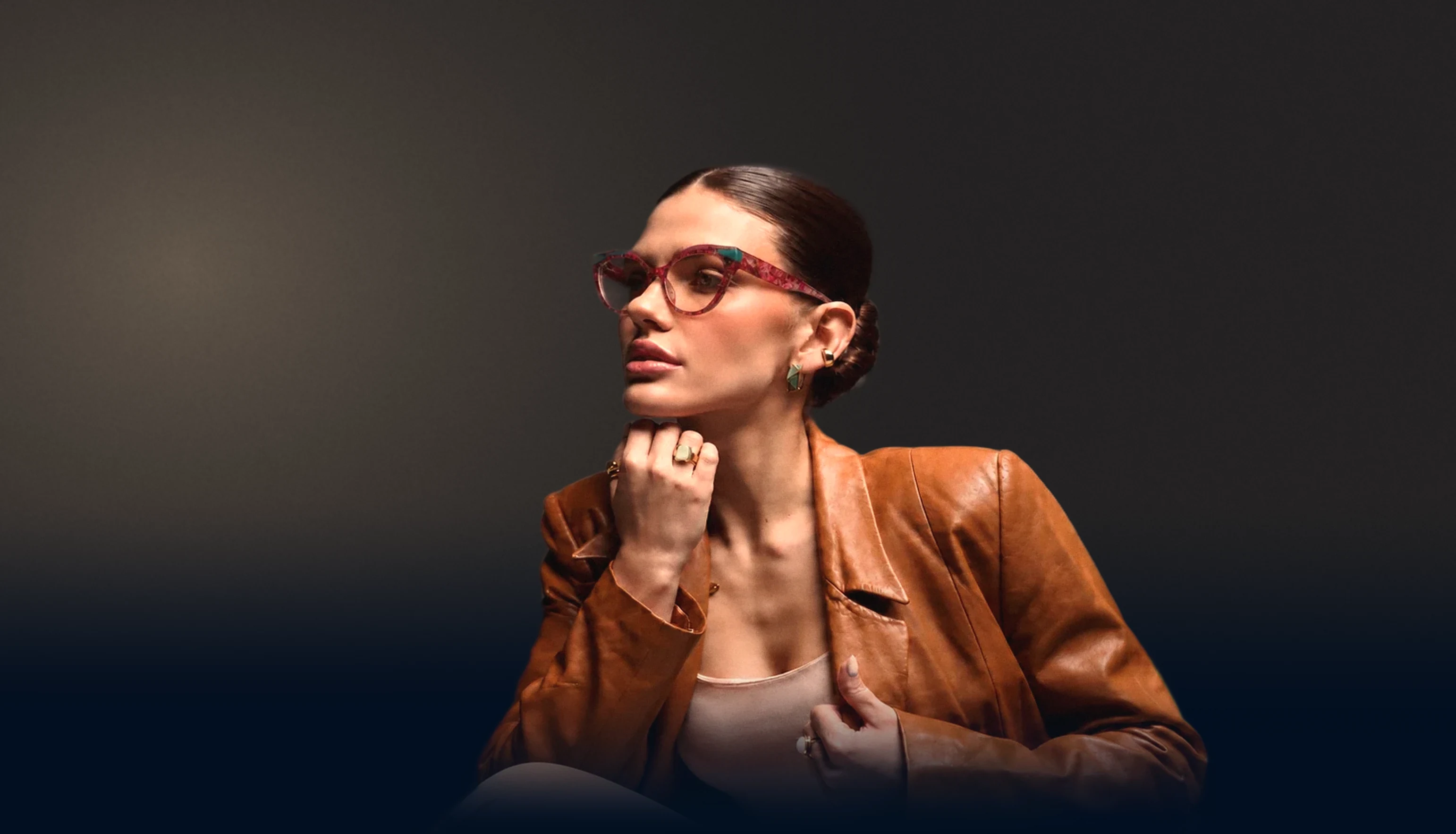 Model in a tan leather jacket wearing pink and turquoise cat-eye glasses